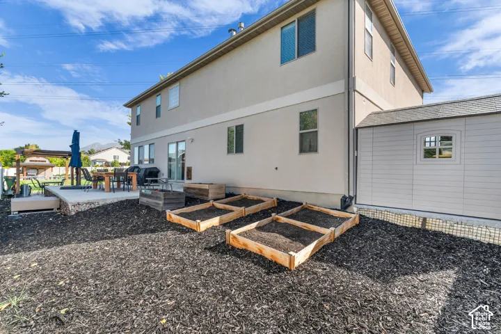 Rear exterior with stucco siding, a concrete patio, a built-in storage shed, and raised garden beds