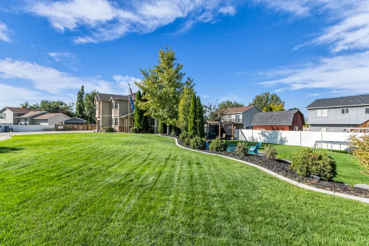 Expansive green lawn with established landscaping beds, a mature deciduous tree, and a white privacy fence