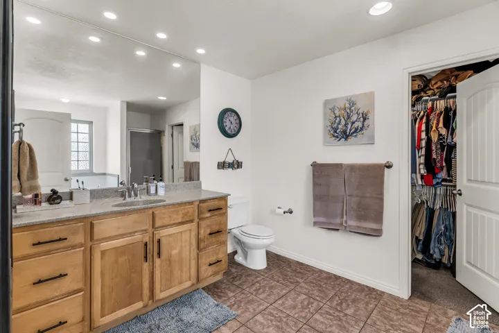 Vanity with extensive storage, stone countertop, tile flooring, built-in recessed lighting, and a walk-in closet
