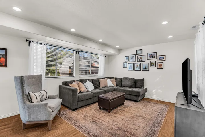Brightly lit living area featuring wood-finish flooring, recessed ceiling lights, and multiple windows with blinds