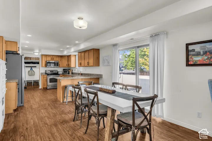 Open-concept kitchen and dining area featuring wood-finish flooring, light wood cabinetry, stainless steel appliances, and a sliding glass door