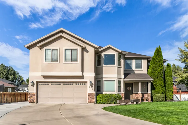Stucco exterior with stone accents, attached garage, covered front porch, bay windows, and a manicured lawn
