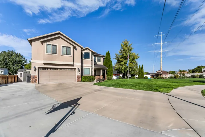 Stucco exterior with stone accents, attached two-car garage, expansive concrete driveway, and a separate storage shed