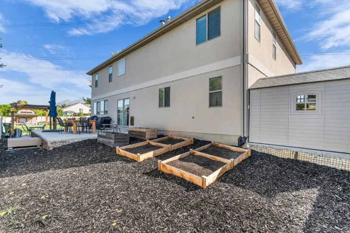 Rear exterior with stucco siding, a concrete patio, a built-in storage shed, and raised garden beds