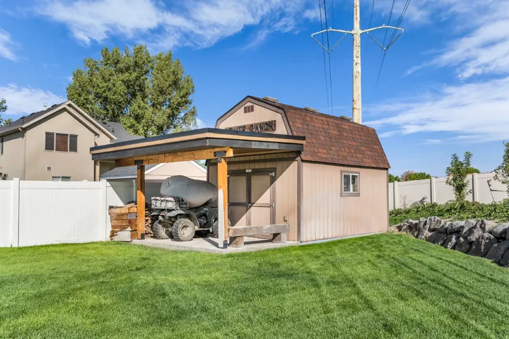 Storage shed with gambrel roof, attached carport with wood beams, and a surrounding vinyl fence
