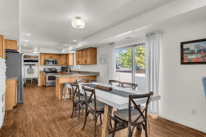 Open-concept kitchen and dining area featuring wood-finish flooring, light wood cabinetry, stainless steel appliances, and a sliding glass door