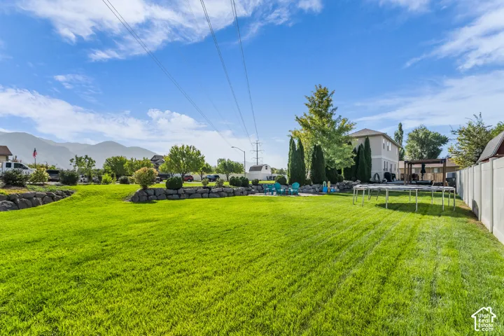 Expansive green lawn, stone retaining walls, mature trees, privacy fencing, and a built-in pergola