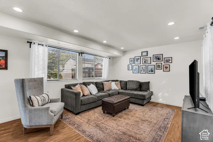 Brightly lit living area featuring wood-finish flooring, recessed ceiling lights, and multiple windows with blinds