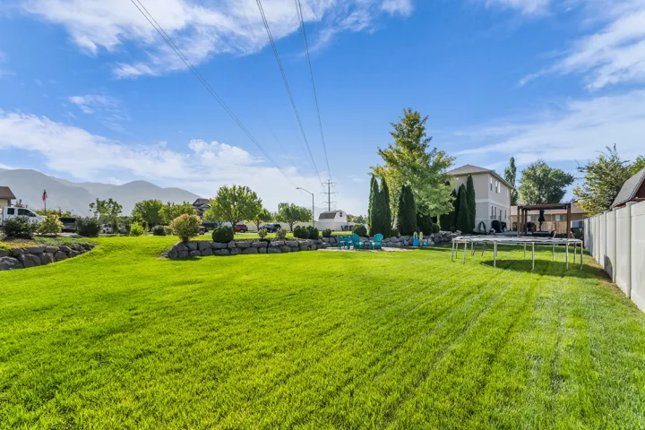 Expansive green lawn, stone retaining walls, mature trees, privacy fencing, and a built-in pergola