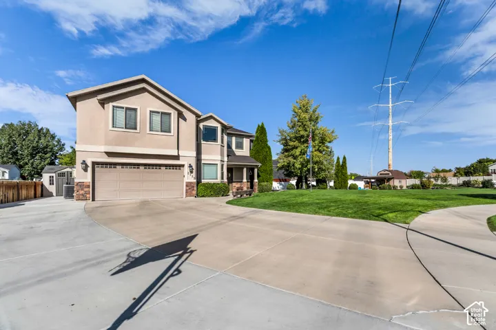 Stucco exterior with stone accents, attached two-car garage, expansive concrete driveway, and a separate storage shed