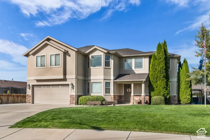 Stucco exterior with stone accents, a two-car garage, covered porch, and mature landscaping