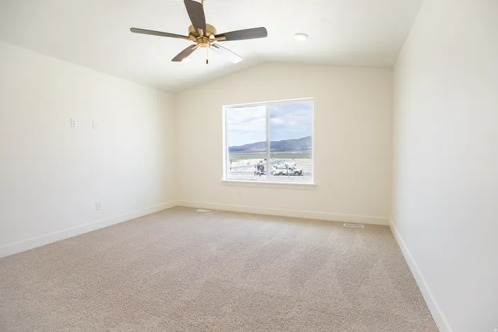 Primary bedroom with vaulted ceiling and ceiling fan, adjacent to large walk-in closet as part of primary suite.