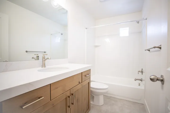 Full secondary bath with stained wood cabinets and quartz slab countertops.