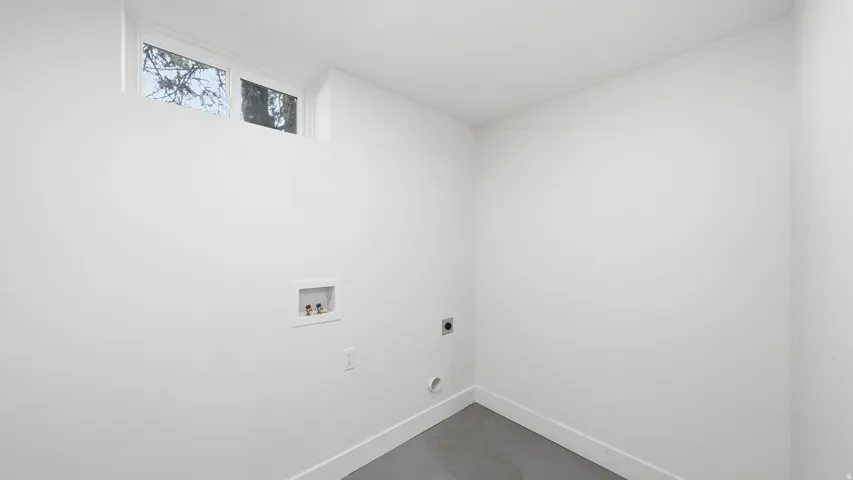 White painted walls with a high transom window, laundry hookups, and a gray floor