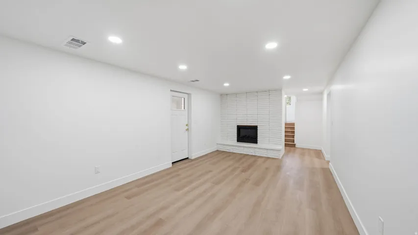 Wood-finish flooring, recessed lighting, white brick fireplace, white door with upper window pane, and painted stairs
