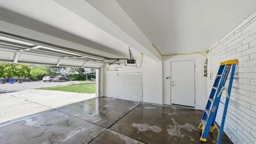 Single-car garage featuring a sectional overhead door, painted brick wall, concrete flooring, and a white access door