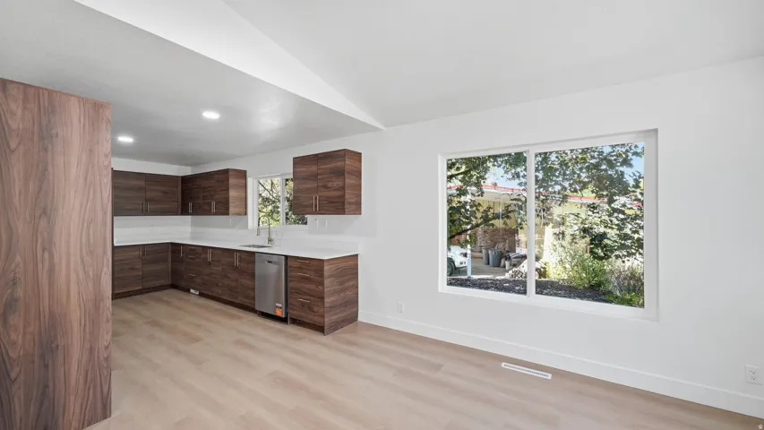 Kitchen featuring wood-finish cabinetry, stainless steel dishwasher, white countertops, tile backsplash, and wood-finish flooring