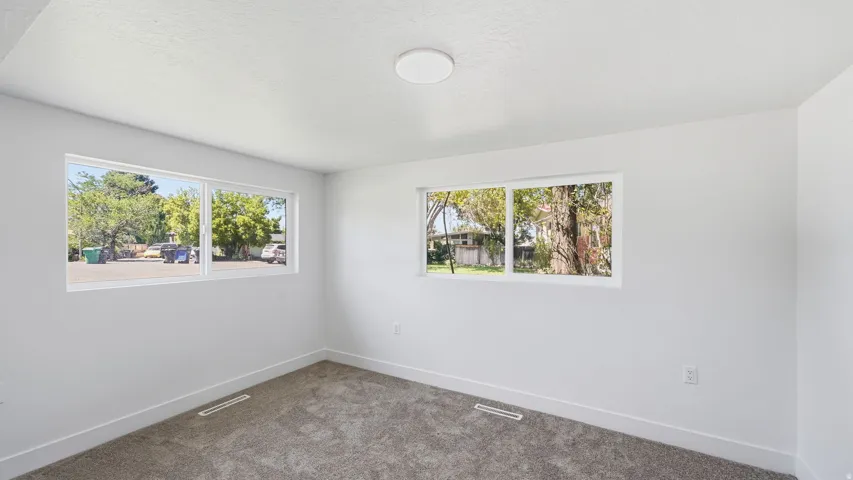 Bright interior space featuring white walls, gray carpet, multiple windows, and a flush-mount ceiling light fixture