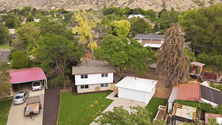 Detached garage, covered carport, mature trees, manicured lawn, and mountain backdrop