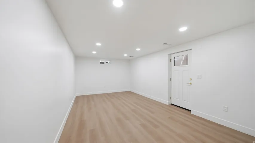 Recessed lighting illuminates the expansive room featuring wood-finish flooring and crisp white walls