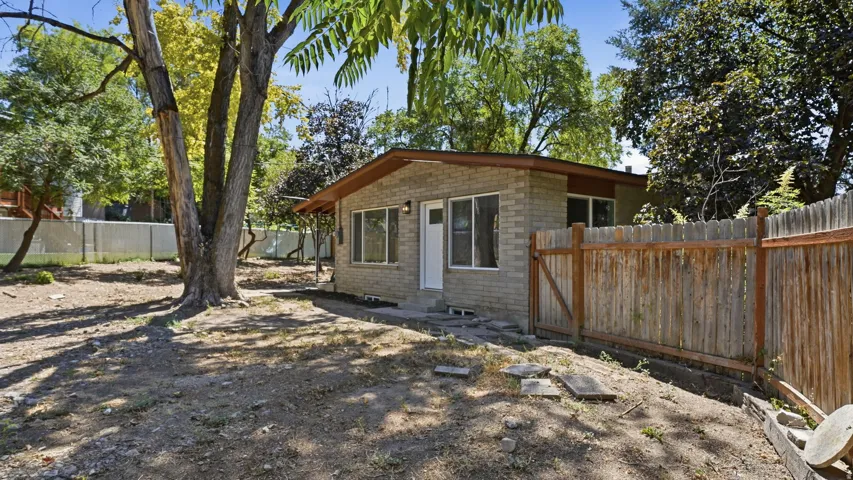 Single-story brick exterior with a wood fence, concrete pathway, and mature trees