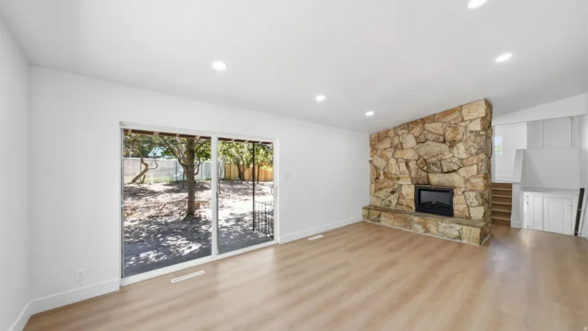 Spacious interior featuring wood-finish flooring, a stone fireplace, recessed lighting, and a sliding glass door to the rear exterior