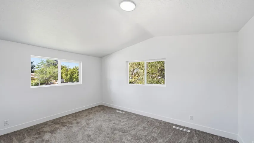Neutral white wall paint, vaulted ceiling, recessed lighting, and grey carpet flooring