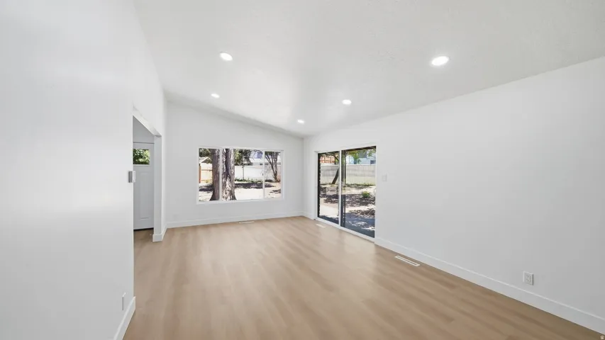 Vaulted ceiling, recessed lighting, wood-finish flooring, large picture window, and glass sliding door