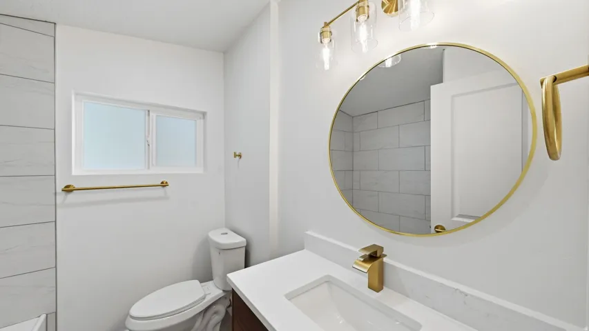 Vanity with a white countertop and integrated sink, gold-finish faucet, and circular mirror