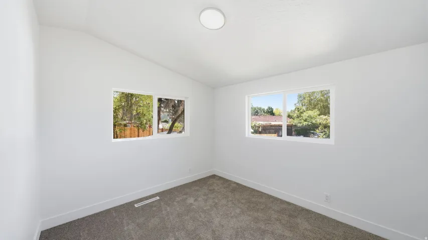 Vaulted ceiling, two windows, recessed ceiling light, gray carpet flooring, white walls