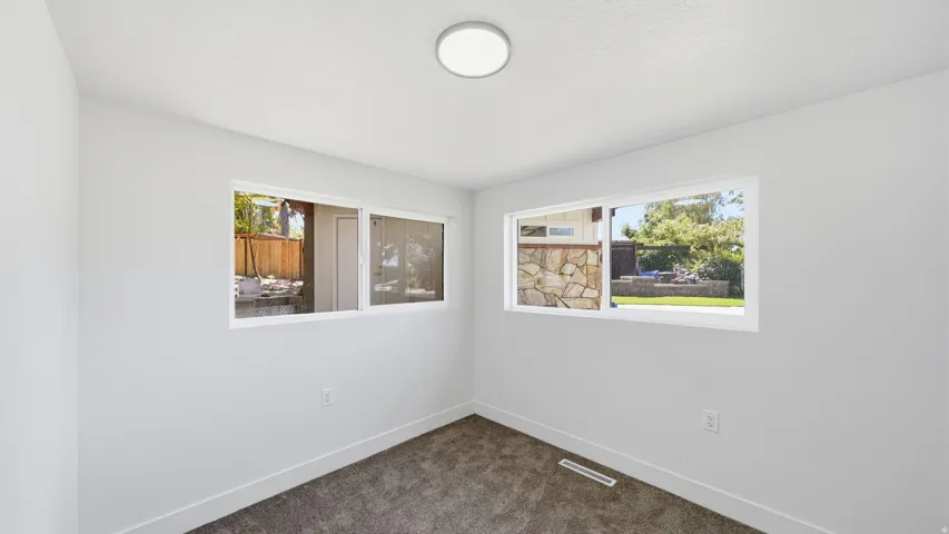 Bright interior with two white-framed windows, recessed lighting, neutral wall finishes, and dark carpeting