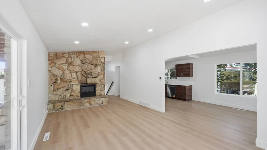 Expansive living area featuring light wood-finish flooring, recessed lighting, and a stone-clad fireplace