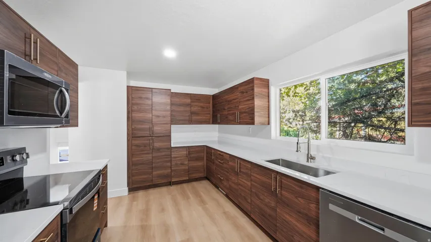 Modern kitchen featuring wood-finish cabinetry, white countertops, stainless steel appliances, and wood-finish flooring