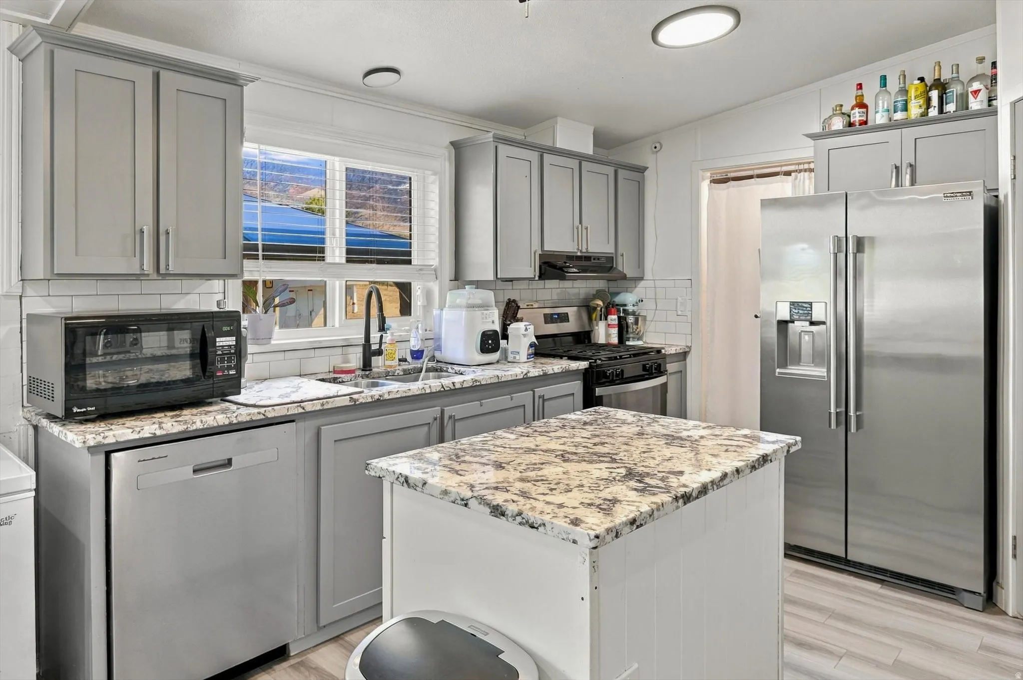 Kitchen featuring grey shaker-style cabinetry, light-toned countertops, subway tile backsplash, and a stainless steel refrigerator