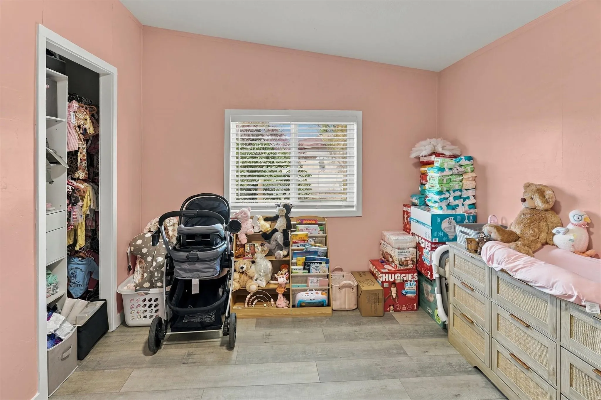 Wood-finish flooring, single window with blinds, sloped ceiling, built-in closet organization, and a wood-tone dresser