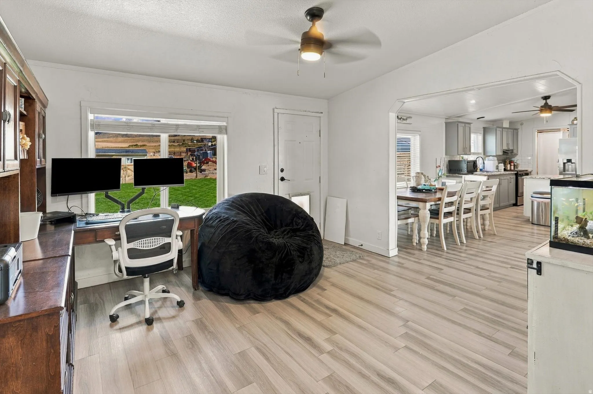 Light wood-finish flooring throughout, bright white walls, and a white ceiling fan with integrated lighting