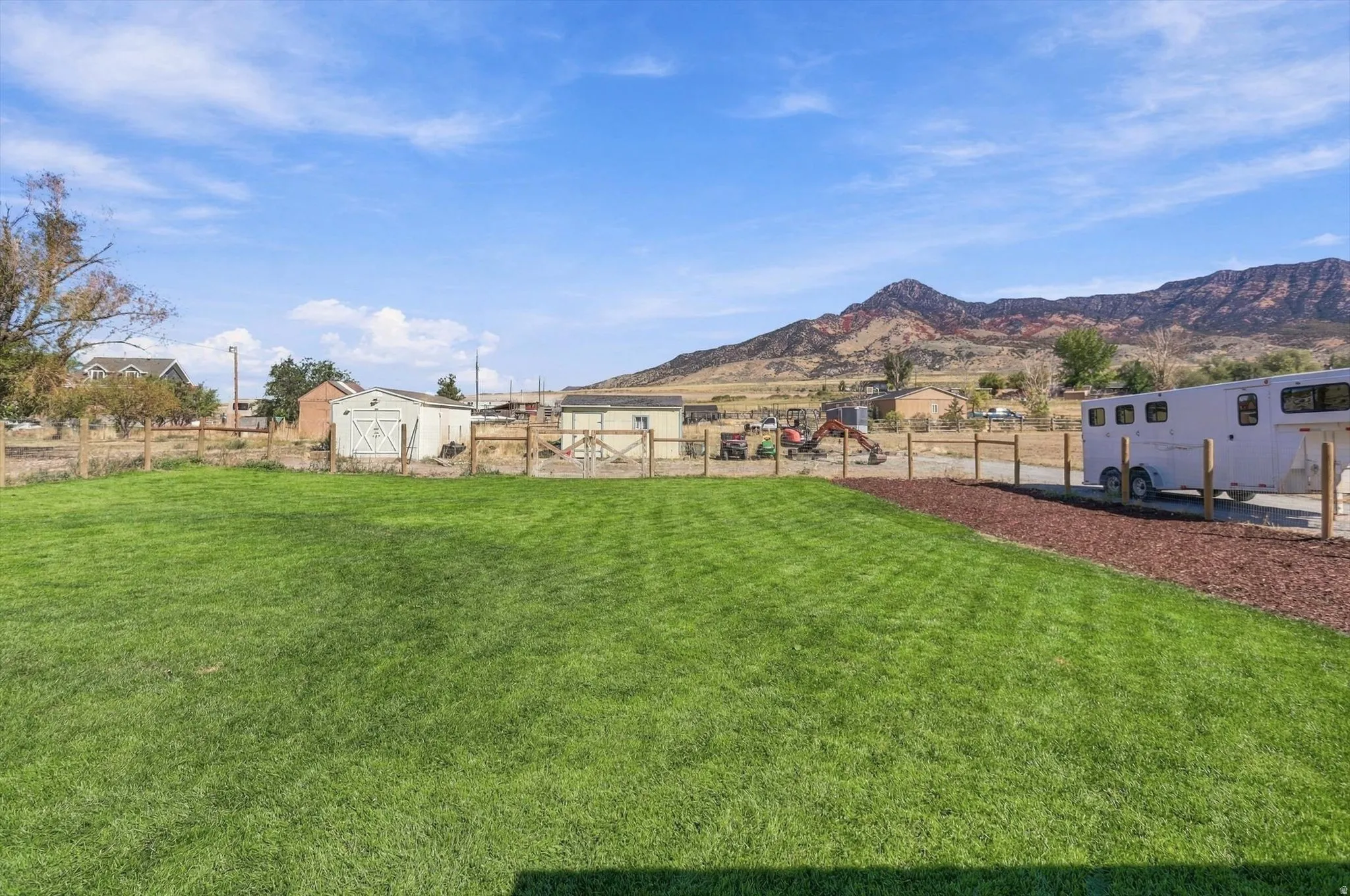 Expansive green lawn with a wood fence, red rock landscaping, and distant mountainous scenery