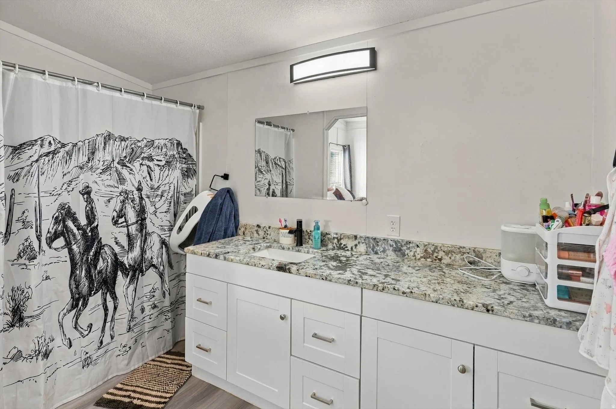 Extended vanity with integrated sink, stone-finish countertop, white cabinetry with silver-tone hardware, and an overhead vanity light