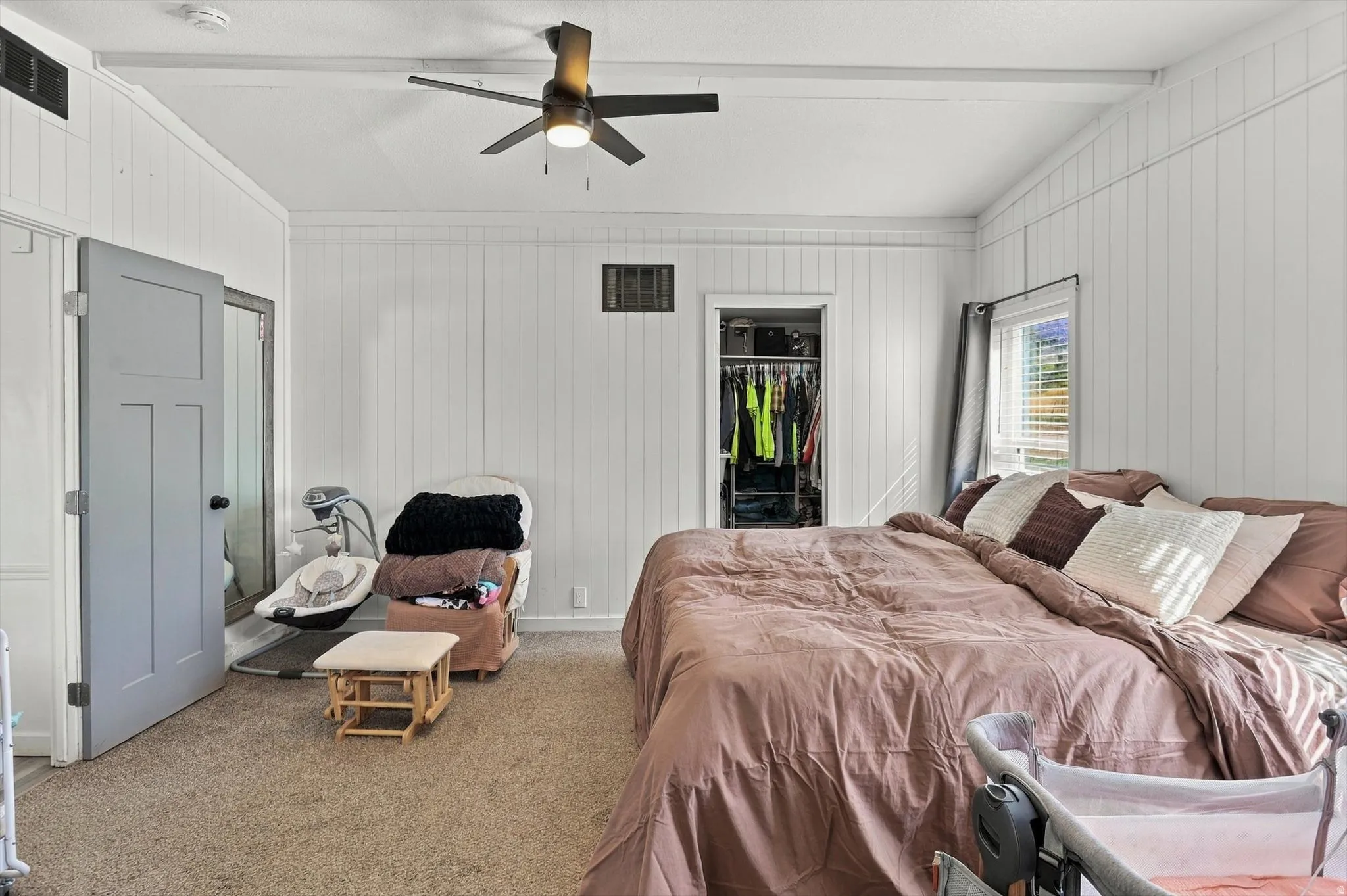 Textured wall paneling, ceiling fan, carpeting, window with blinds, and a built-in closet with shelving