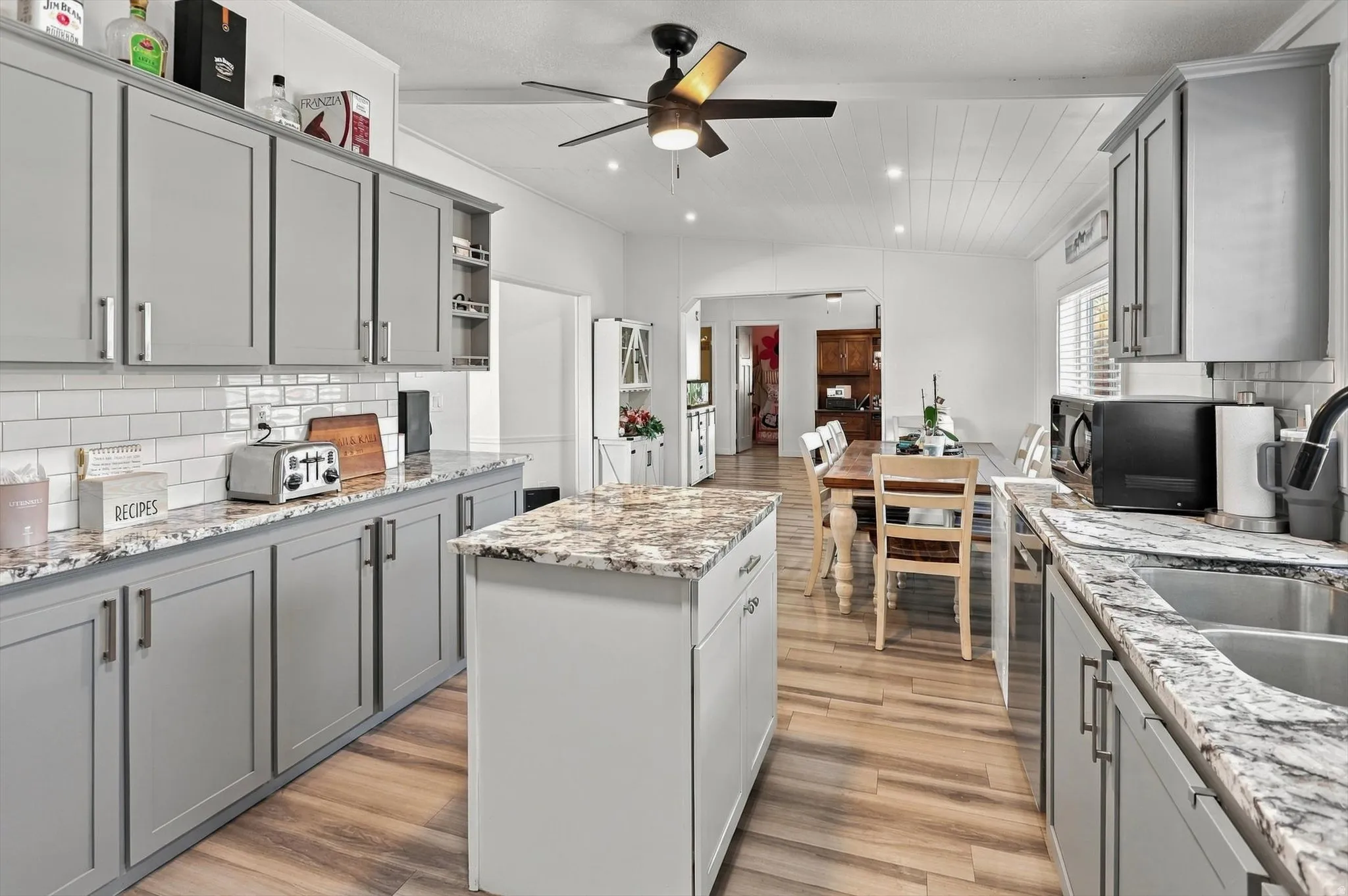 Kitchen featuring wood-finish flooring, gray cabinetry, a central island with a stone countertop, subway tile backsplash, and recessed lighting