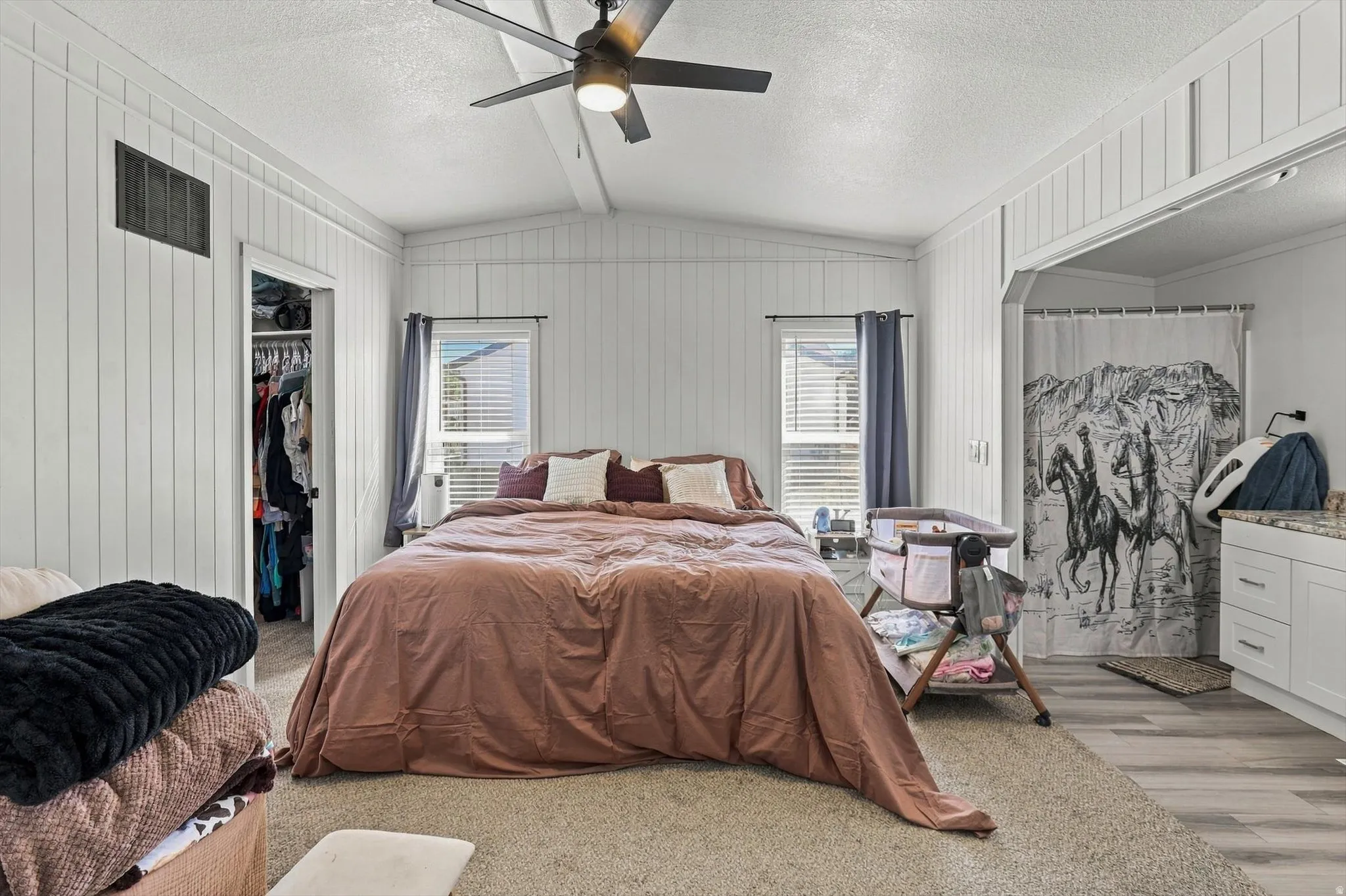 Vaulted ceiling with a ceiling fan, white vertical paneling, two windows with blinds, built-in closet, and light-toned carpet