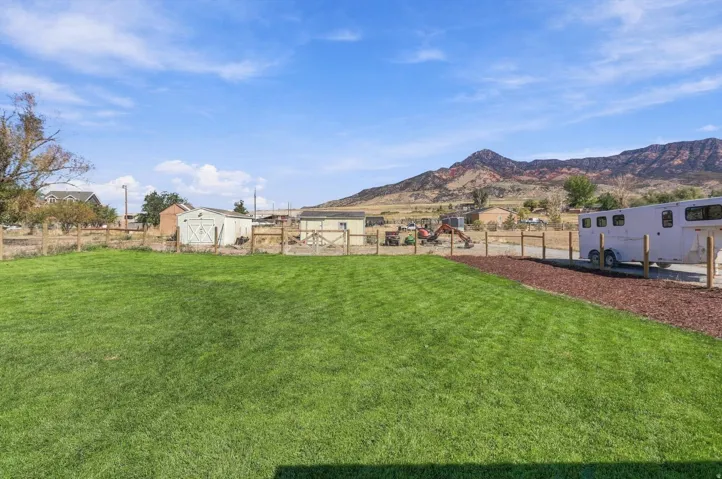 Expansive green lawn with a wood fence, red rock landscaping, and distant mountainous scenery