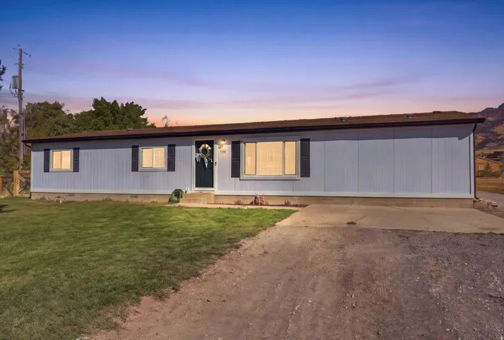 Light blue siding with dark shutters, front door with sidelights, a small concrete porch, and a gravel driveway
