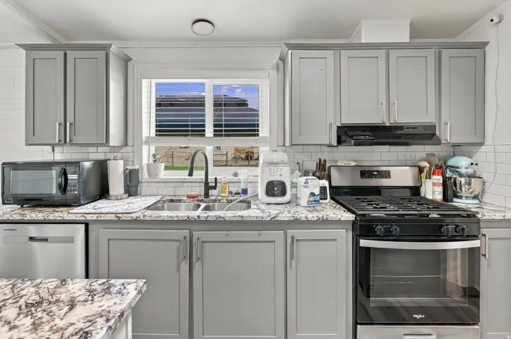 White subway tile backsplash, gray cabinetry, stainless steel dishwasher, dual basin sink with gooseneck faucet, and a stainless steel gas range