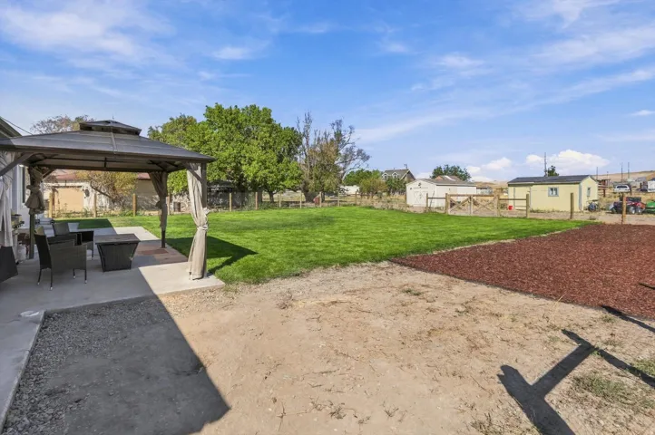 Expansive exterior featuring a concrete patio, a covered gazebo, a large grassy area, a mulched section, and a wood fence
