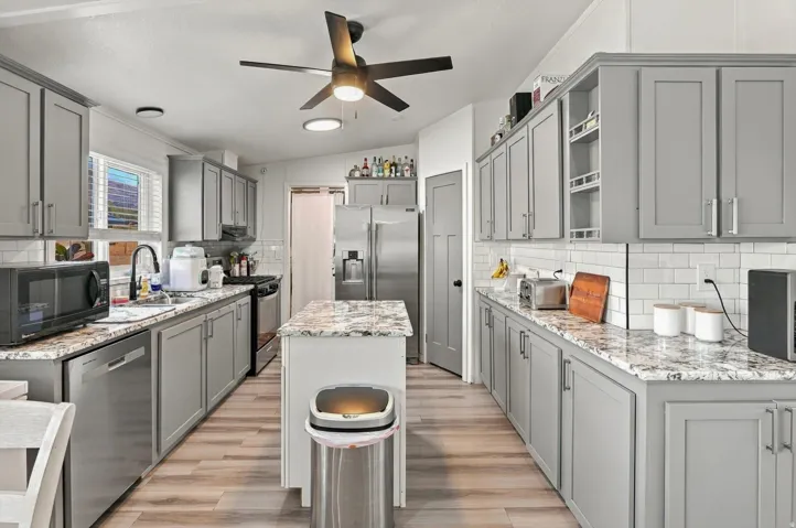 Kitchen featuring wood-finish flooring, gray shaker-style cabinetry, a white subway tile backsplash, and stone countertops