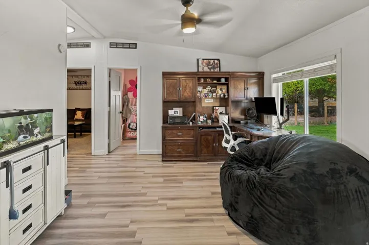 Vaulted ceiling, ceiling fan, wood-finish flooring, built-in wood cabinetry, sliding glass door to exterior