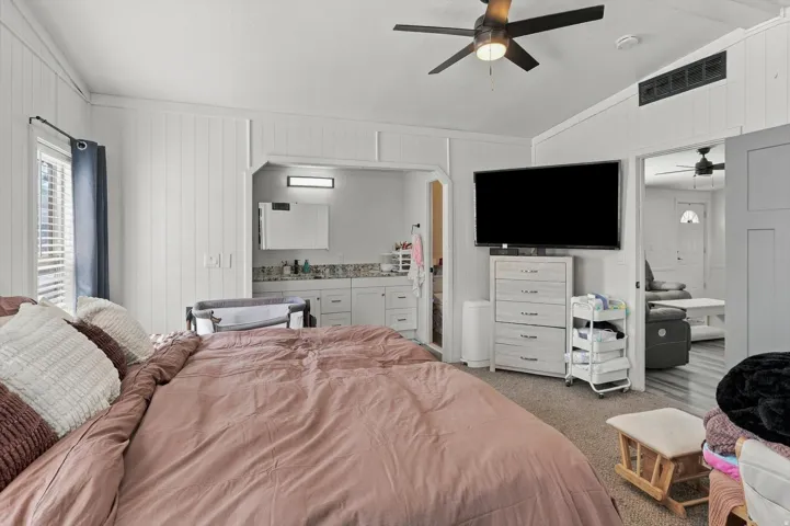 Carpeted bedroom with a ceiling fan, vertical paneling, and an en-suite vanity area featuring white cabinetry and a countertop