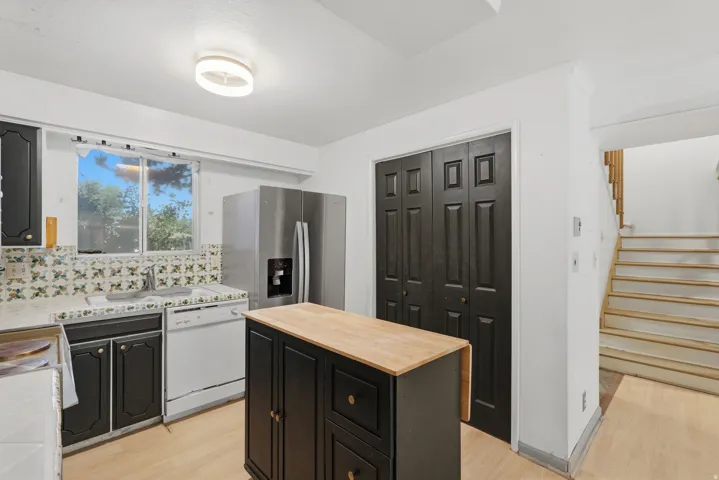 Kitchen featuring dark cabinetry, a freestanding stainless steel refrigerator, white dishwasher, and a patterned tile backsplash