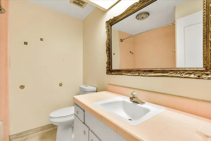 Vanity with an integrated ceramic sink, tile countertop, ornate framed mirror, and a built-in toilet